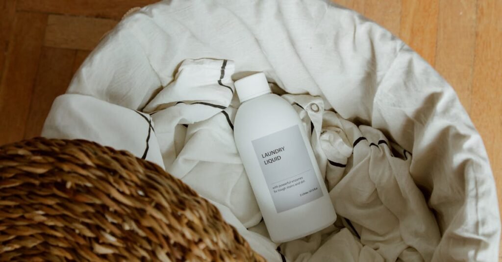 High angle view of laundry liquid in basket with white linens on wooden floor.