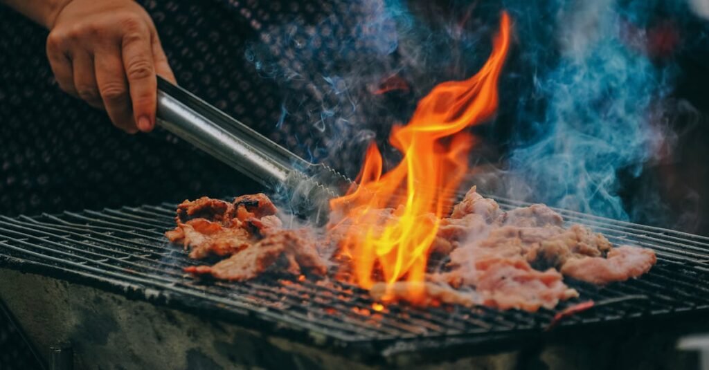 Close-up of grilling meat with vibrant flames and smoky aura, showcasing outdoor cooking.