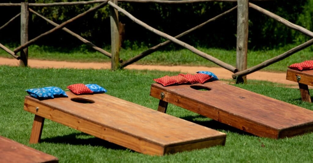 Wooden cornhole boards with colorful bean bags on a green lawn during a sunny day outdoors.