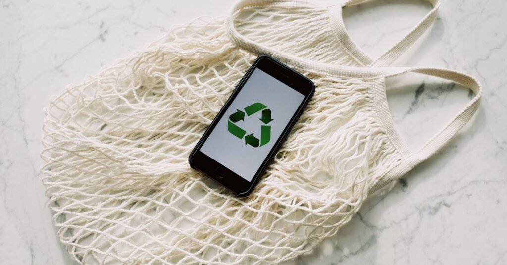 Overhead of smartphone with simple recycling sign on screen placed on white eco friendly mesh bag on marble table in room