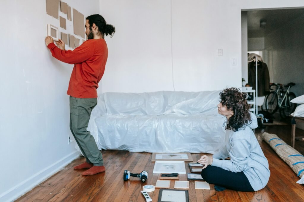 A couple decorates their new home living room by arranging picture frames on the wall.