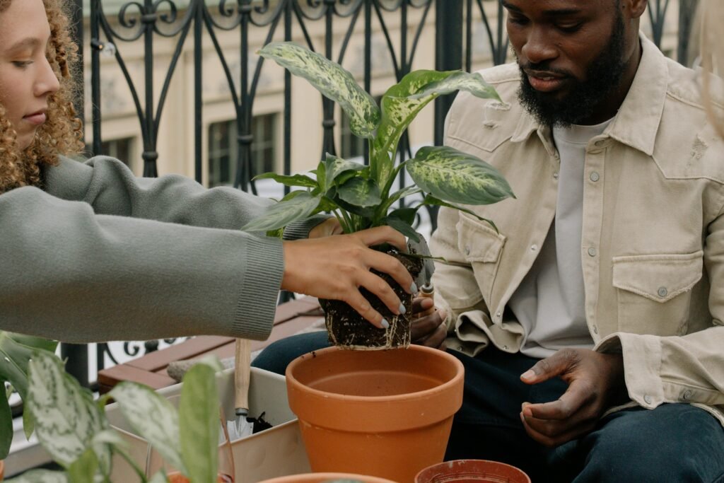 Two friends enjoy urban gardening on a balcony, planting in terracotta pots.